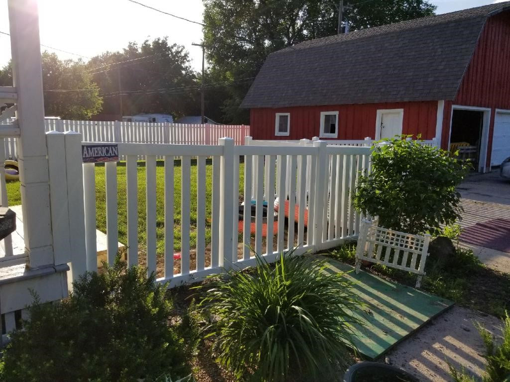 White picket fence and a red barn with potted plants in the foreground.