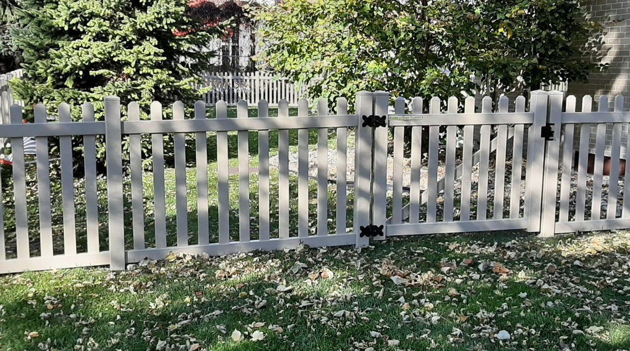 A white picket fence with black hinge in a garden strewn with decaying leaves.